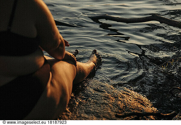 Tiefschnitt einer jungen  üppigen Frau  die bei Sonnenuntergang am Wasser sitzt