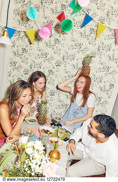 Tilt shot of young multi-ethnic friends enjoying dinner party sitting at apartment