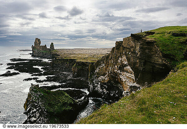 Tiny people on grand cliff with clouds and rock formations on coast