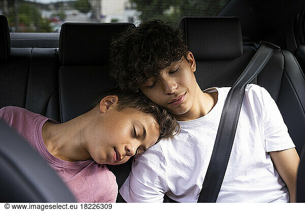 Tired brothers leaning on each other while resting in car