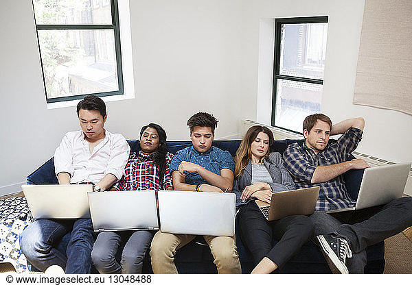 Tired business people using laptop while reclining on sofa in office