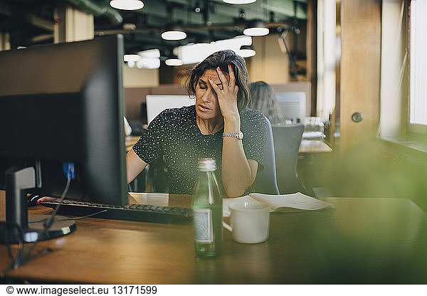 Tired businesswoman with head in hand sitting at computer desk in office