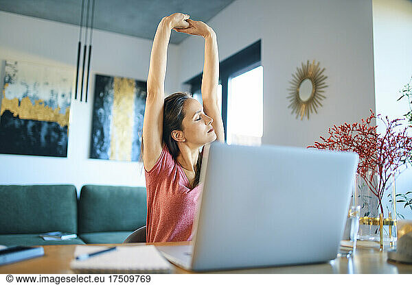 Tired female freelancer stretching arms while sitting in home office