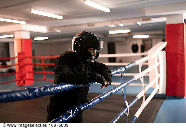 Tired fighter in protective gear resting on boxing ring