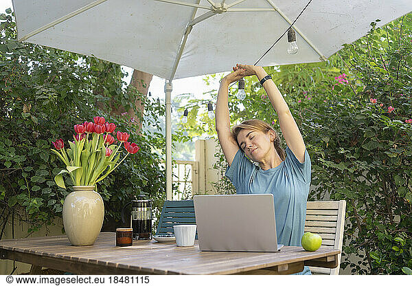 Tired freelancer stretching arms sitting at table in garden