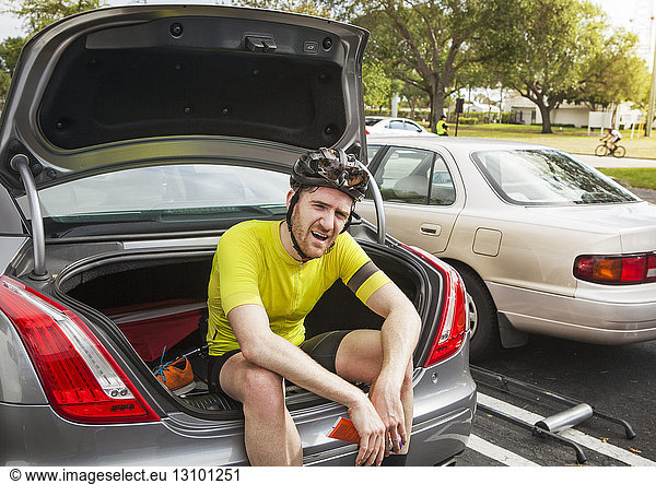 Tired male cyclist sitting in car trunk