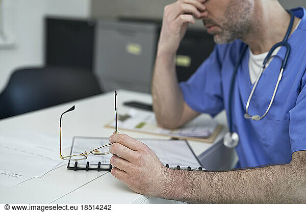 Tired mature doctor sitting at desk in clinic
