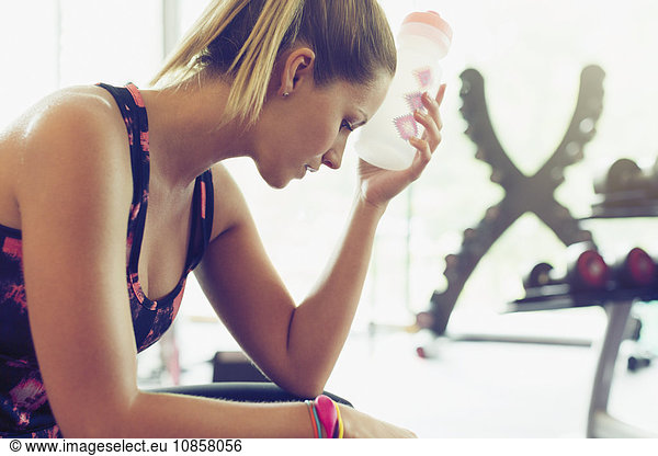 Tired woman cooling forehead with water bottle at gym