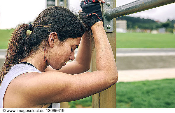 Tired woman leaning against gymnastics bar at park