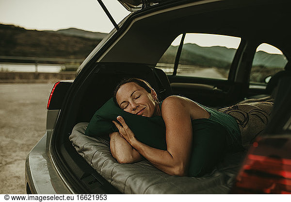 Tired woman sleeping in cozy car trunk at dusk