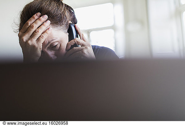 Tired woman talking on telephone at laptop