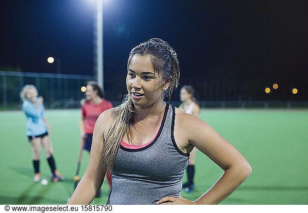 Tired young female field hockey player resting on field at night