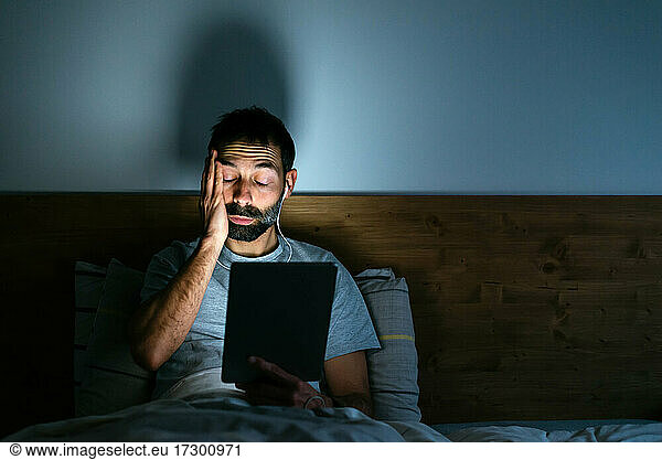 Tired young man wiping eyes while working at tablet
