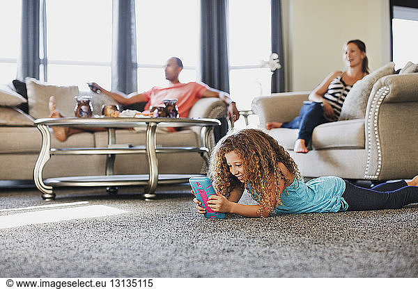 Tochter spielt Handheld-Spiel  während die Eltern zu Hause fernsehen