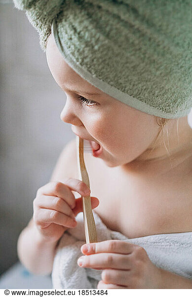 Toddler baby with a towel on her head brushes teeth wooden