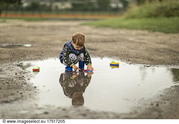 Toddler blonde boy plaing in puddle and his reflection