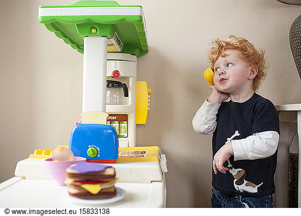 Toddler boy answering phone in his play kitchen with cute expression