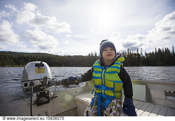toddler boy driving motorboat on lake.