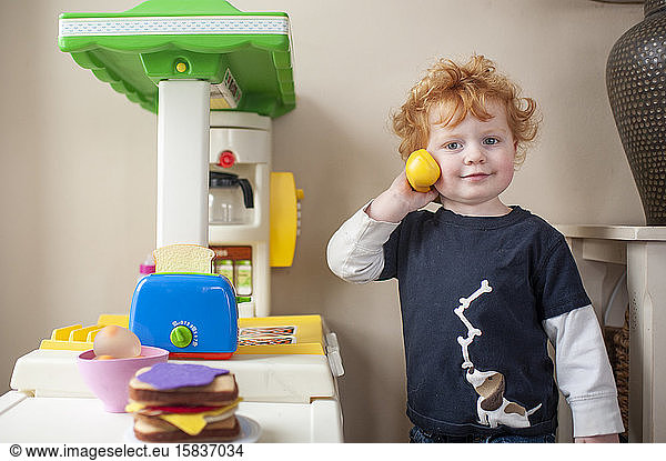 Toddler boy looking while answering phone in play kitchen at home