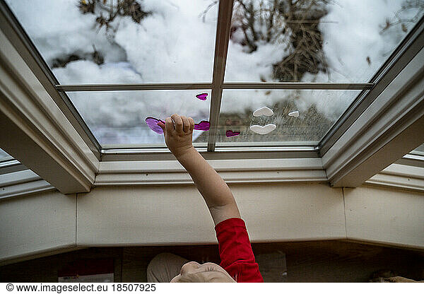 Toddler Boy Placing Window Cling Heart on Window for Valentine's Day