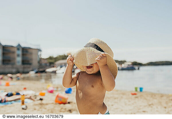 Toddler Boy Playing Peek-a-boo with Sun Hat on Beach