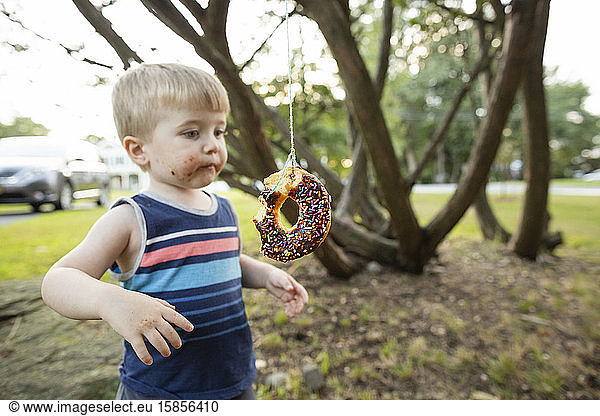 Toddler boy stands next to donut hanging from string during party