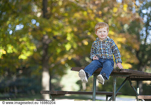 Toddler boy 3 to 4 years old sitting on edge of picnic table smiling