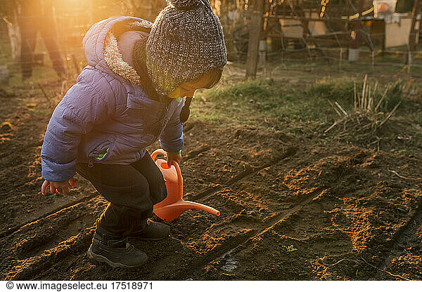 Toddler boy watering freshly planted plants with orange watering