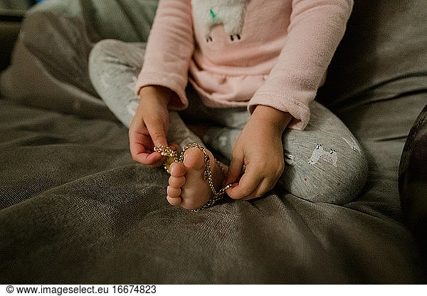 Toddler girl playing with bead necklace. with her feet