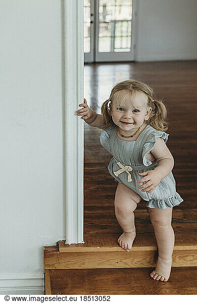 Toddler girl smiling at camera while walking down stairs in a studio