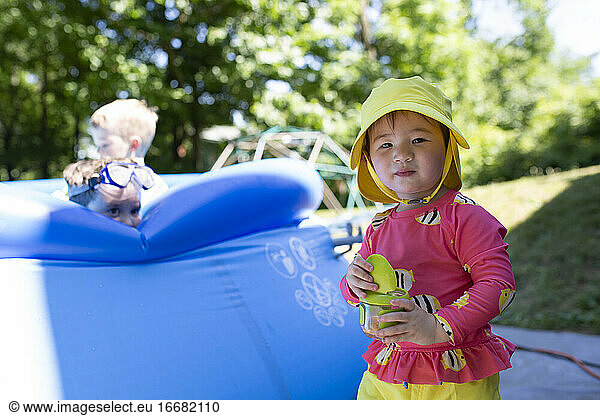 Toddler Girl Wearing Yellow Sun Hat Eats Snack Next To Backyard Pool