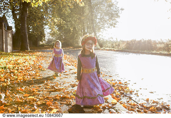 Toddler girls in Halloween costumes walking in autumn leaves