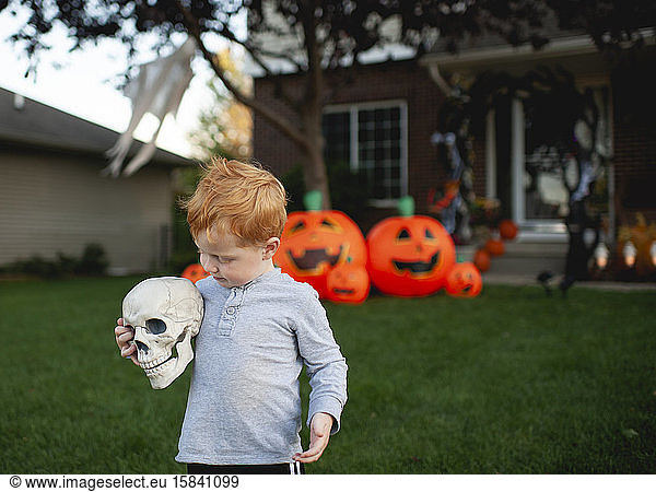 Toddler holding skeleton head in front of outdoor halloween decor