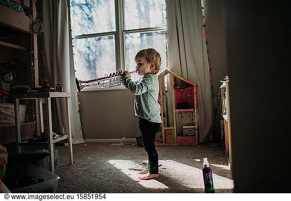 toddler in bedroom playing toy trumpet