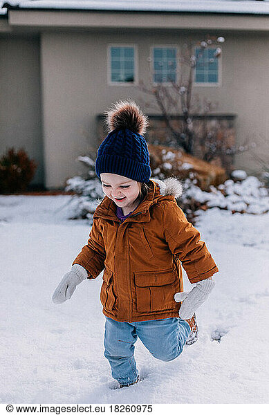 Toddler in mittens running through a snow covered yard smiling