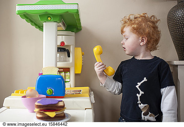 Toddler looking at phone in play kitchen with cute expression at home