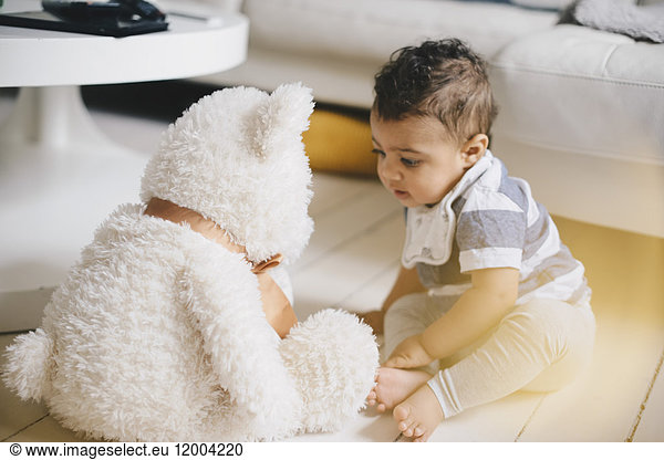 Toddler looking at teddy bear while sitting on floor at home