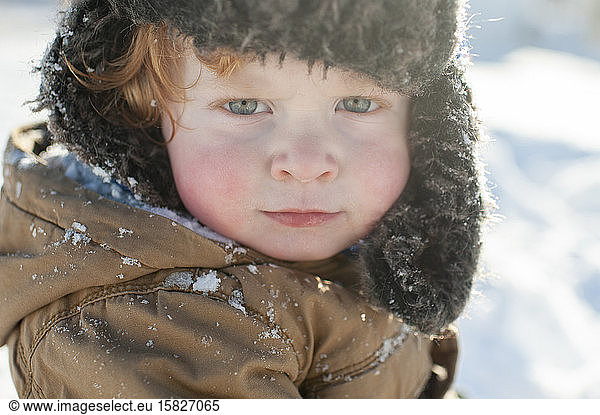 Toddler making serious face in winter hat and jacket in the snow