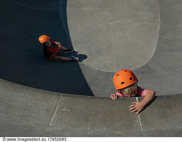 Toddler skateboarders in orange helmets at the skatepark