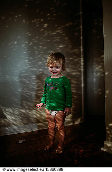 toddler standing in hallway with dots of sunlight sparkles