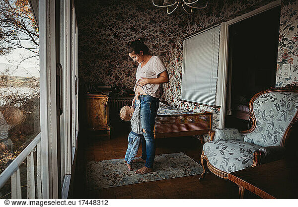 Toddler touching mom's belly in vintage room with wallpaper