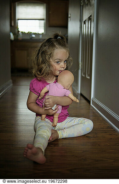 Toddler with curly hair and blue eyes hugging and kissing baby doll