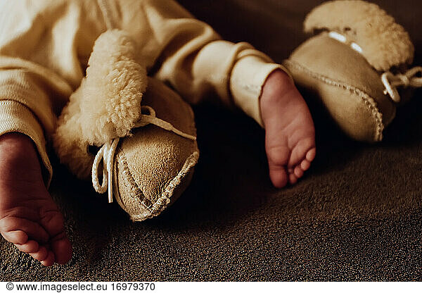Toes of newborn baby with beige sheepskin booties and thermo pants