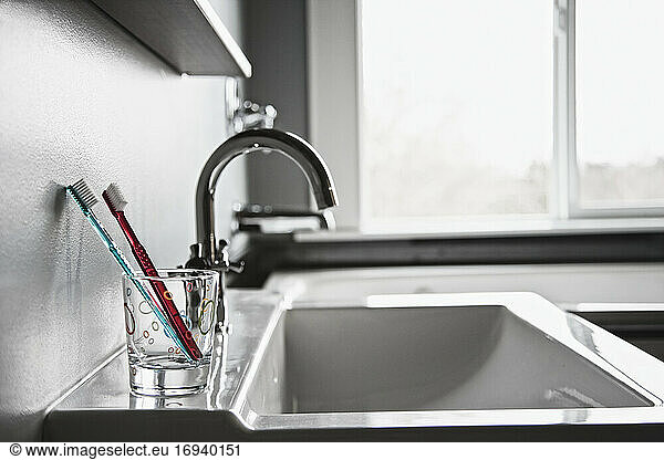 Toothbrushes in drinking glass in domestic bathroom.