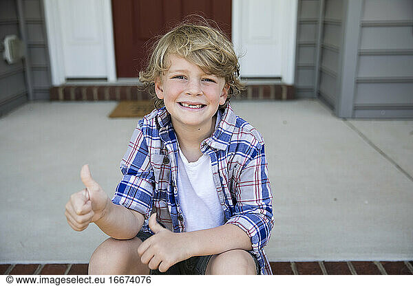 Toothless First Grade Boy Gives Thumbs Up While Sitting on Brick Steps