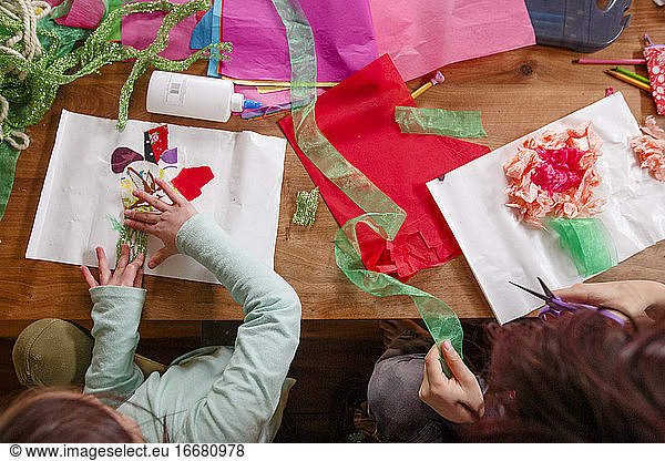 Top-down view of two children doing arts and crafts at a wooden table
