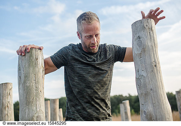 Top-half of man leaning on wood poles on obstacle course