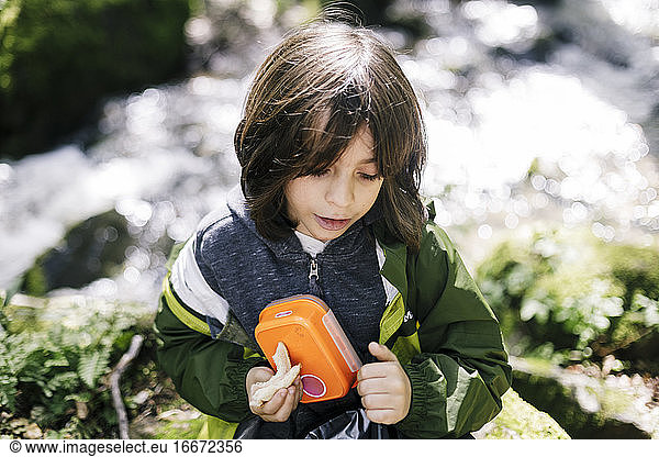 Top view of child holding his lunch container by river in natural park