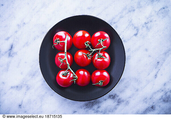 Top view of fresh tomatoes on black plate against marble