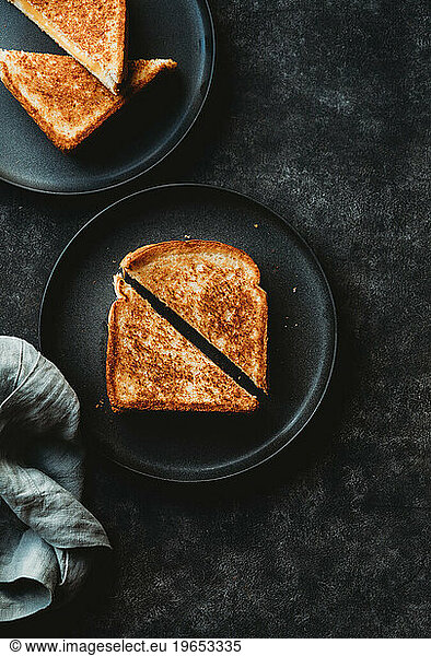 Top view of grilled cheese sandwiches on black plates and background.